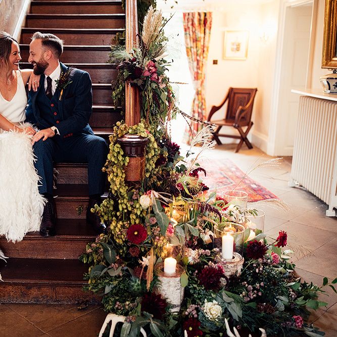 Bride Sitting on The Stairs  in a Charlie Brear Payton Bridal Gown &amp; Piora Feather Skirt with Her Groom in a Navy Suit