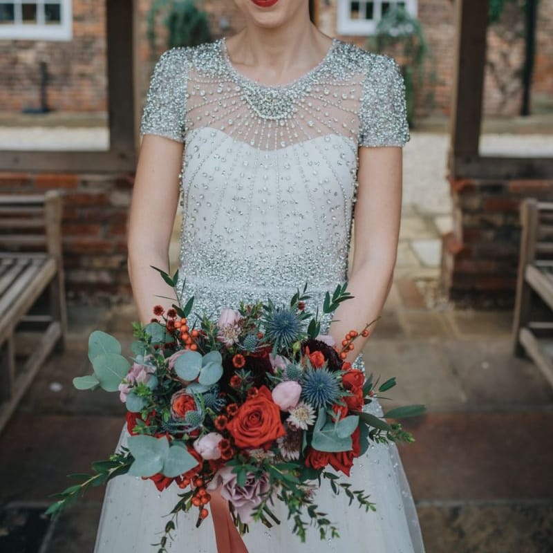 Close up detail of brides embellished wedding dress teamed with a red lip and a festive floral bouquet