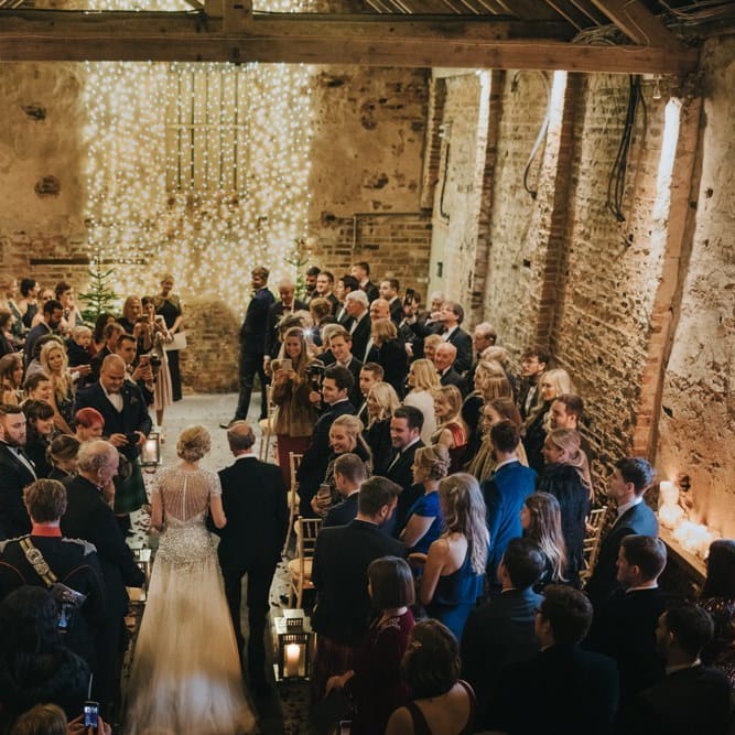Winter ceremony with candle lantern aisle and a fairy light curtain with Christmas trees