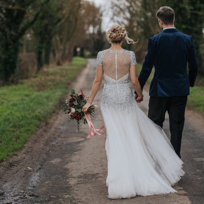 Back of brides embellished wedding dress with groom wearing a navy velvet suit at winter wedding