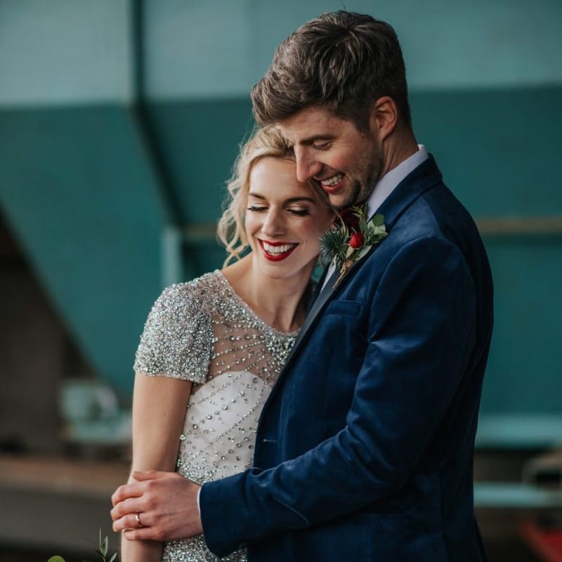 Bride and groom embrace at winter wedding wearing an embellished wedding dress and navy velvet suit