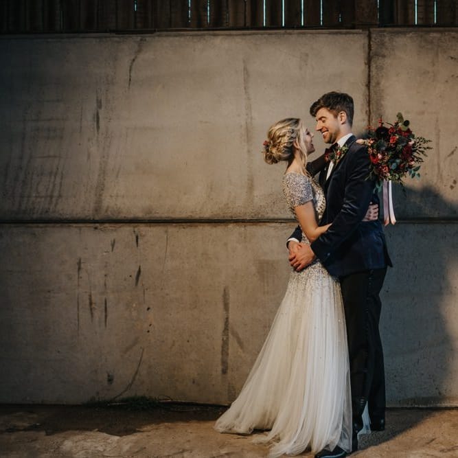 Bride and groom embrace at winter wedding wearing an embellished wedding dress and navy velvet suit