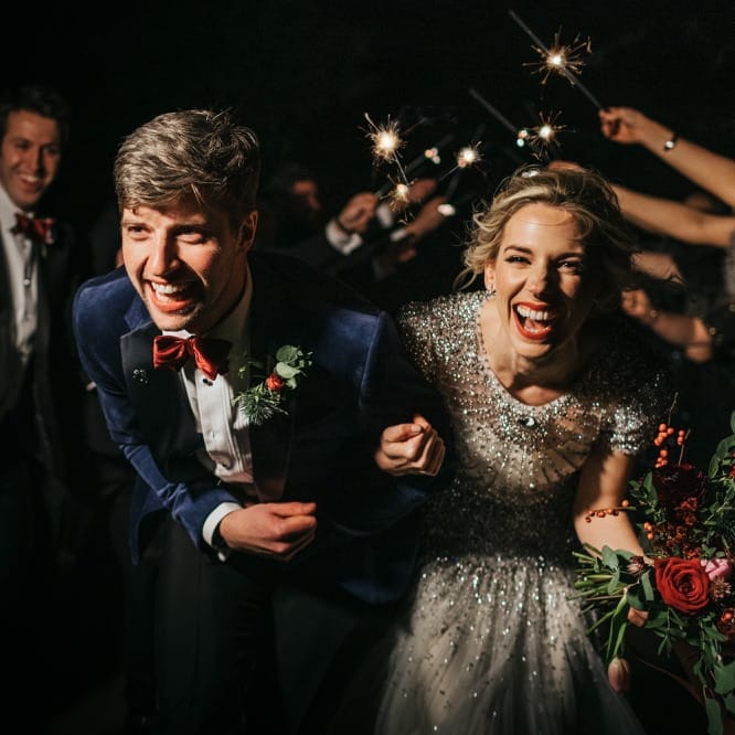 Bride and groom confetti exit wearing embellished wedding dress and red rose floral bouquet