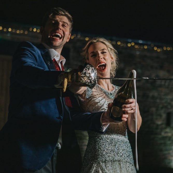 Bride and groom using a sword to open a bottle of champagne at winter reception
