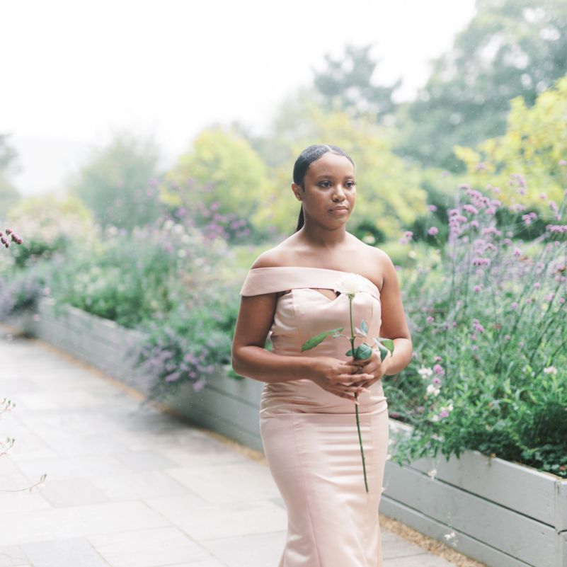Bridesmaid in off the shoulder pastel dress holding a single flower stem