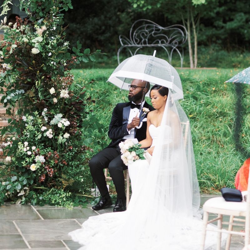 Bride and groom sitting under a clear umbrella during the outdoor wedding ceremony