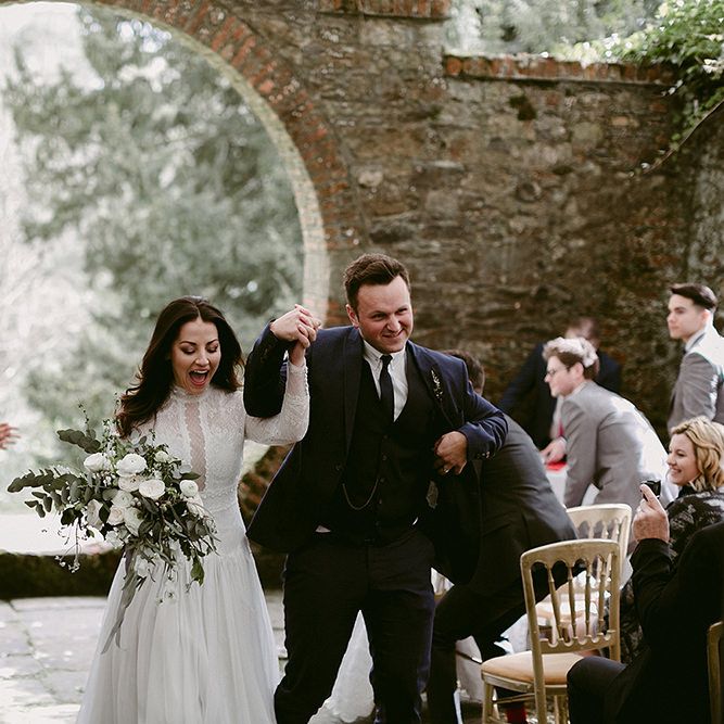Bride in a Homemade Wedding Dress with Lace Bodice and Long Sleeves and Groom in Navy Suit Walking Up the Aisle