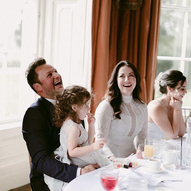 Bride in Homemade Wedding Dress with High Neck and Long Sleeves Laughing During The Speeches with Her Groom in Zara Suit