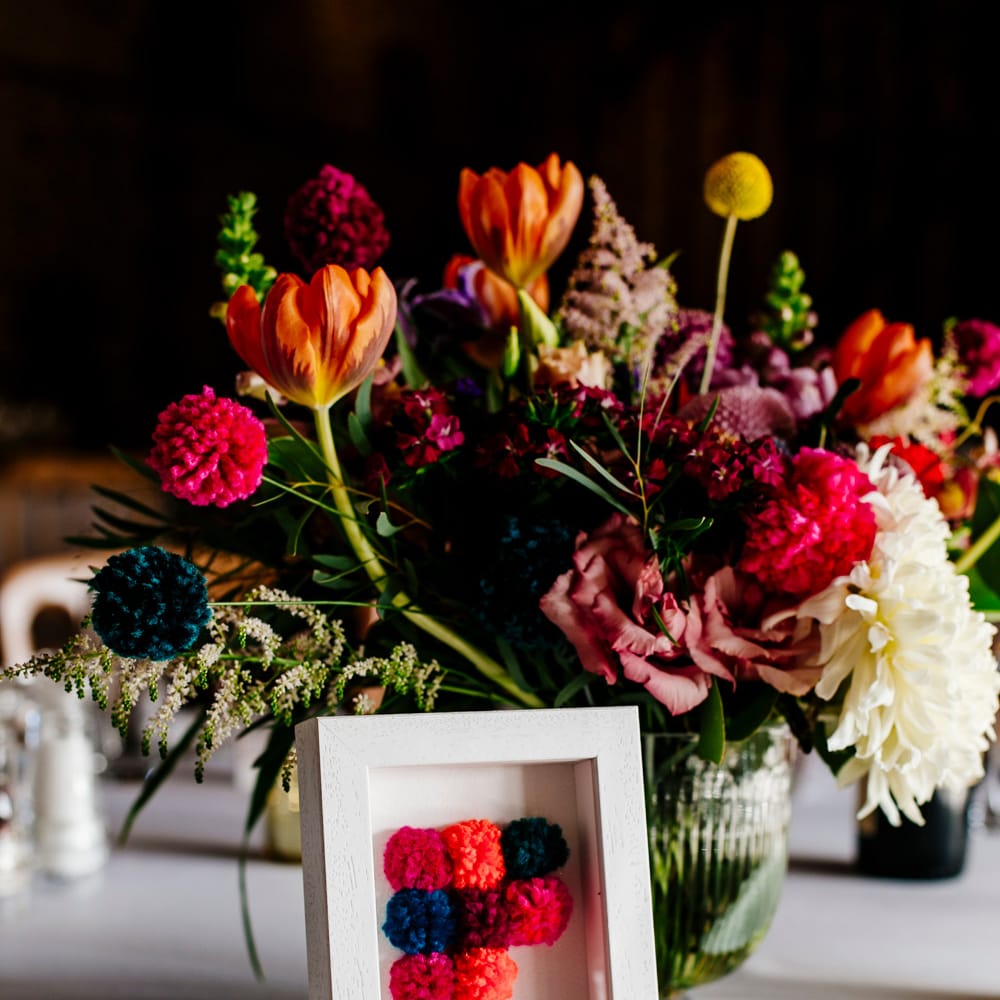 Table Centrepiece with Pom Pom Table Number | Colourful Alternative Winter Wedding at Upwaltham Barns, Sussex | Epic Love Story Photography