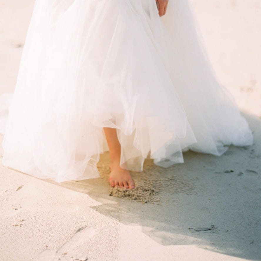 Bride in tulle wedding dress walking on the beach