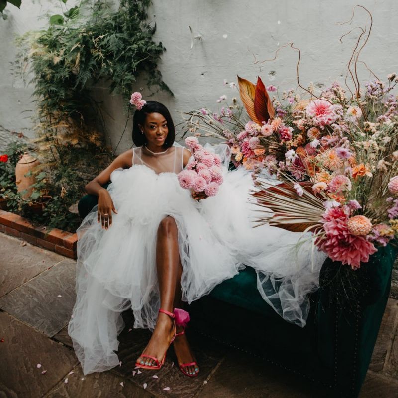 Bride in tulle wedding dress sitting on a flower filled sofa at Secret Garden Kent
