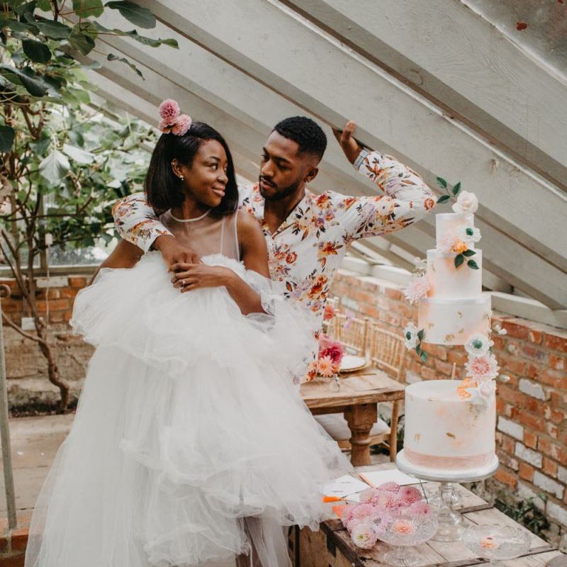 Bride in tulle wedding dress and groom in floral shirt cutting the wedding cake at tropical wedding