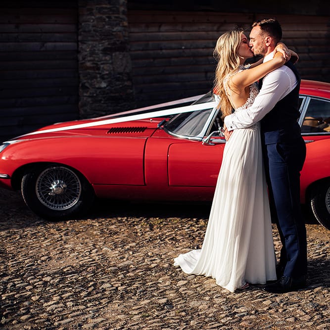 Bride and groom embracing in front of a red sports car