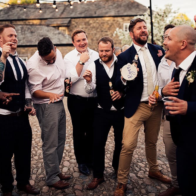 Groomsmen gathered in the courtyard with tambourines and beers