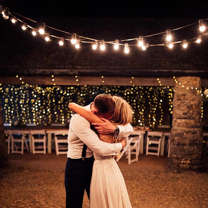 Bride and groom embracing under festoon lights