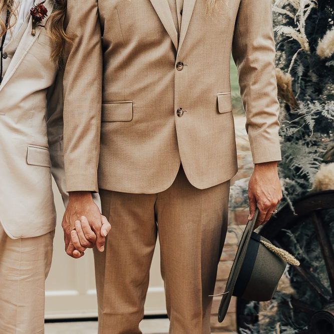 Two grooms holding hands in light coloured suits