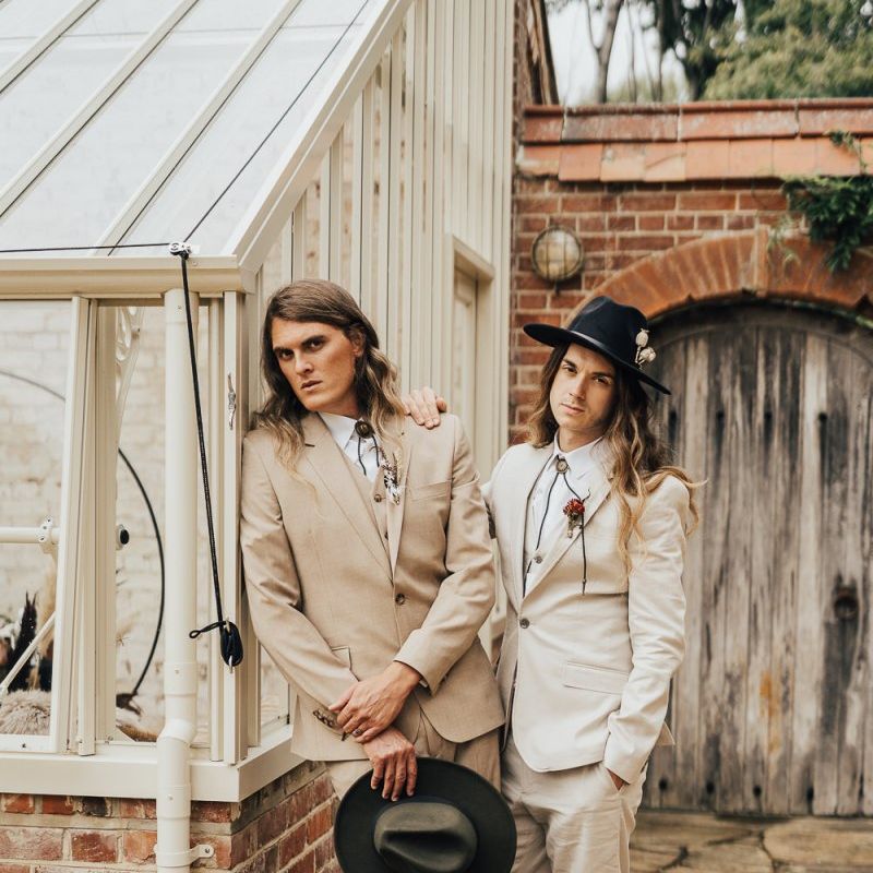 Two grooms with hats standing outside a glasshouse