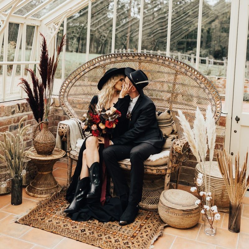 Bride in black wedding dress and hat kissing her groom in a conservatory