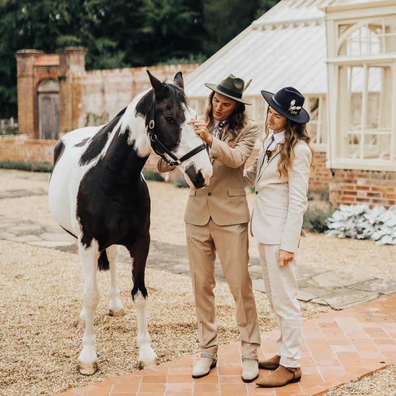 Grooms in neutral suits and black hats with a horse at a western wedding