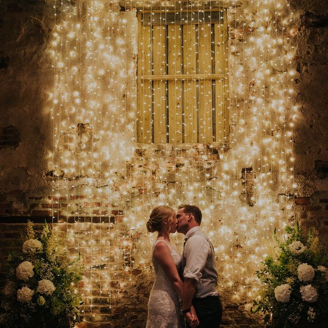 Bride and Groom Kissing in Front of Fairy Light Backdrop