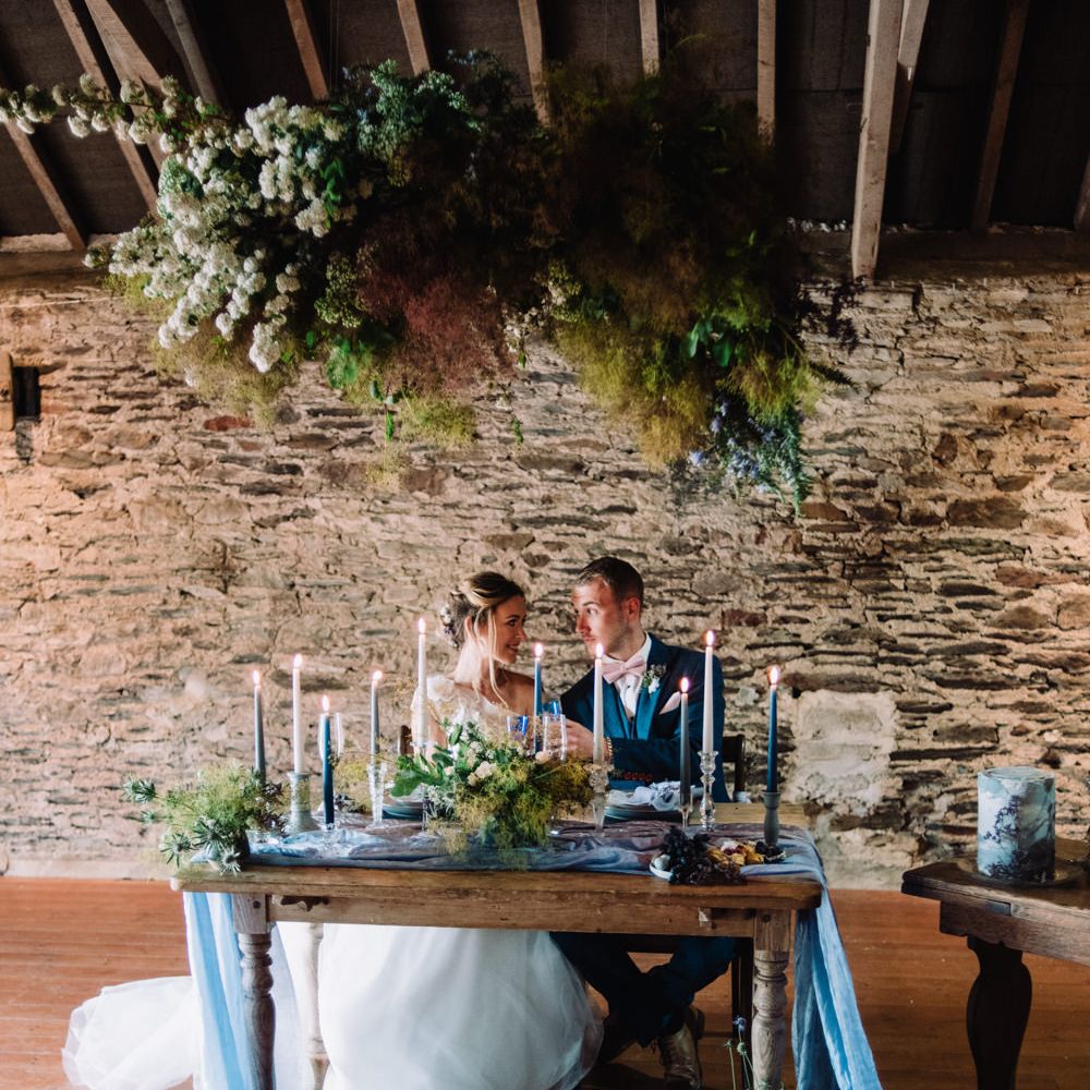 Elegant Tablescape with Floral Installation, Blue Taper Candles &amp; Linens | Bride in Ghost Wedding Dress | Groom in Navy The Vintage Suit Hire Co. Suit | Wild Coastal Elopement, Bridal Inspiration at New Barton Barns, Devon | Liberty Pearl Photography &amp; Film