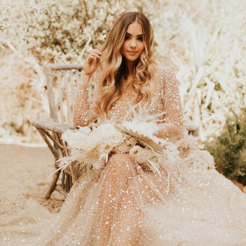 Boho bride in sparkly wedding dress with wavy hair and dried flower bouquet