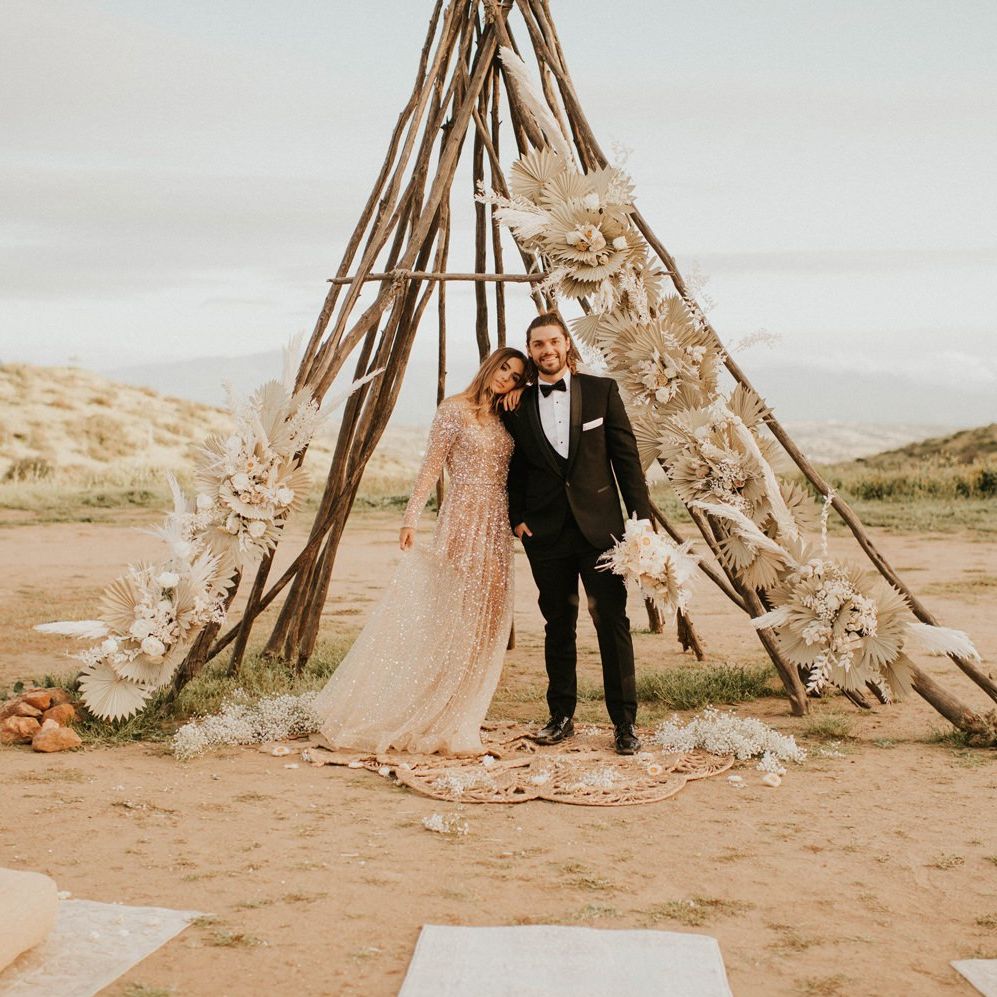 Boho bride and groom standing in from of a naked tipi structure