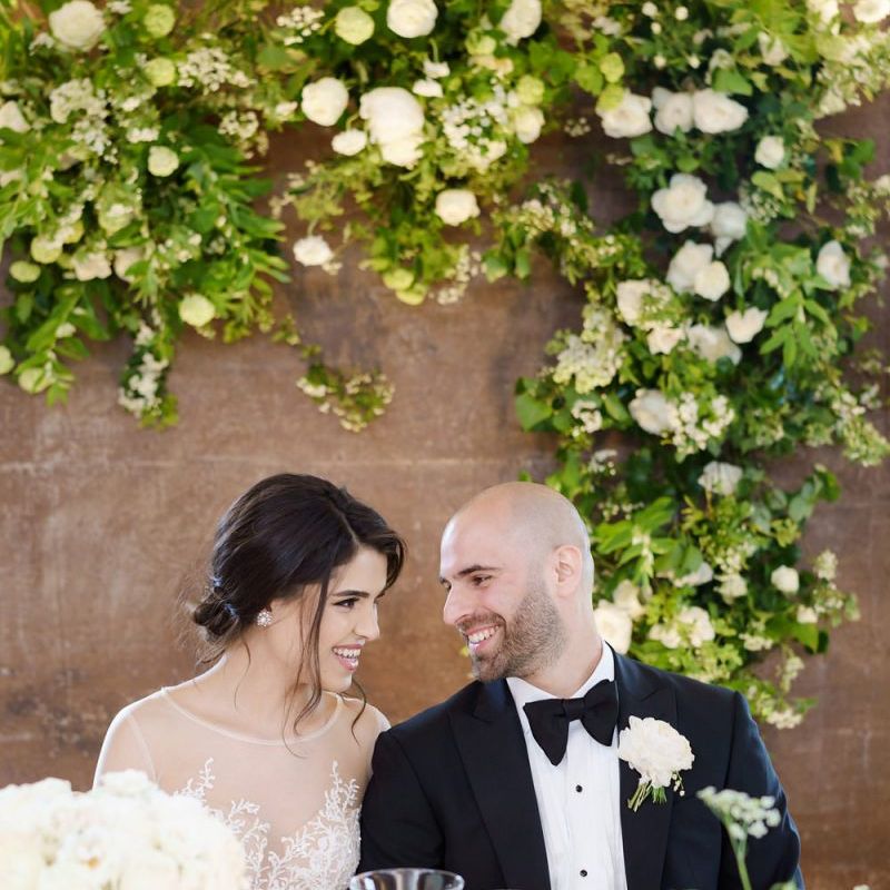 Bride and Groom Sitting at the Top Table with Green and White Wedding Flowers