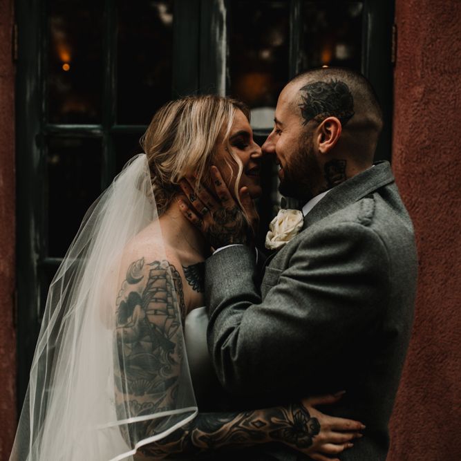 Tattooed Bride with Sweetheart Wedding Dress and Groom in Highland Wear Embracing Her Face