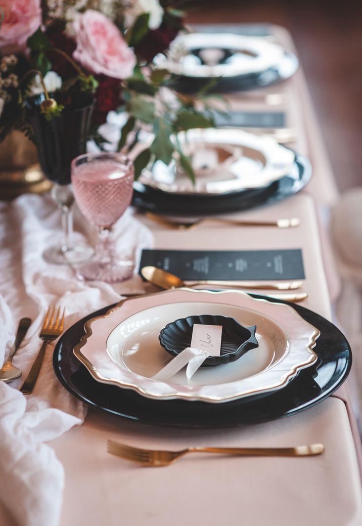 Place setting with black and gold rimmed tableware, and an ornate shell plate 