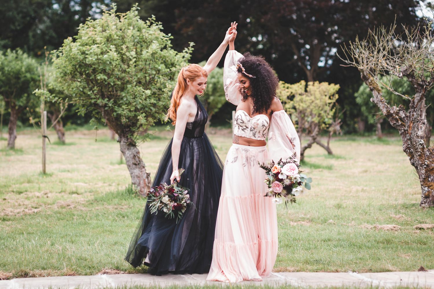 Wedding portrait of an neurodiverse couple in a black tulle wedding dress and blush pink separates dancing in a field 