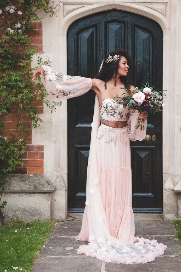 Black bride with long naturally curly hair in a blush pink with embroidery detail bridal three-piece including bodice, skirt and blouson sleeves 