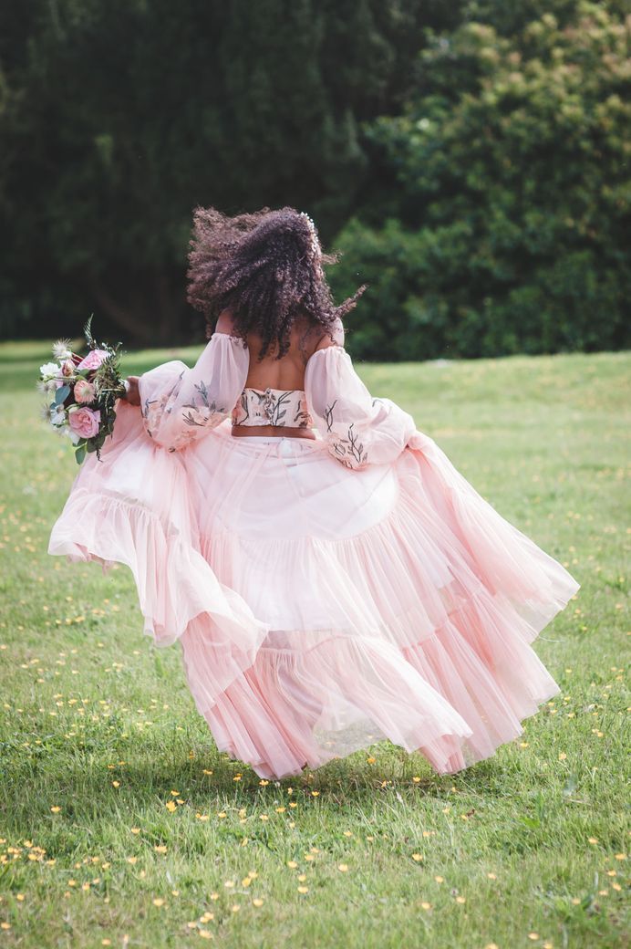 black bride with long naturally curly hair running in a garden in blush pink bridal separates with tulle skirt, embroidered bodice and detachable sleeves 