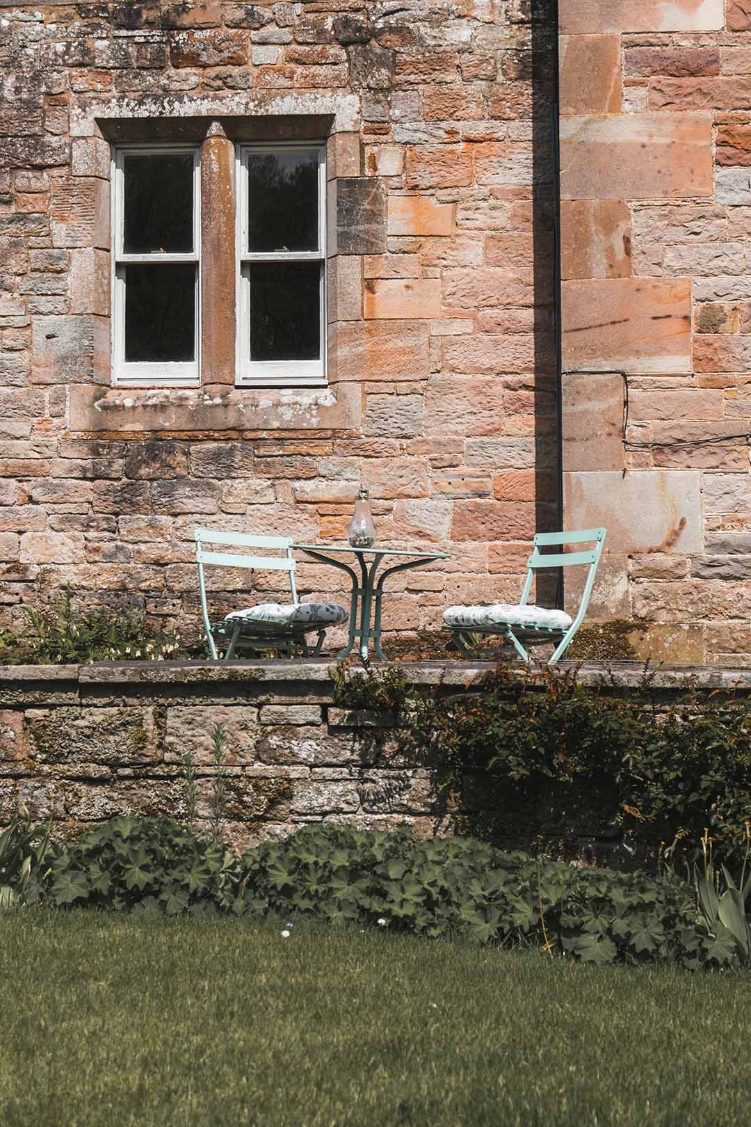 Image of a UK country style house with a table and chairs set up outside 