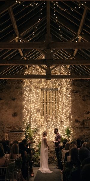 Bride and groom exchange vows in front of cascading fairy lights in The Normans wedding venue Ceremony Barn