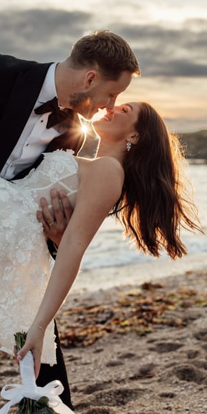 A bride and groom kiss in front of a sunset on a Devon beach. Captured by Fox and Co Photography. 