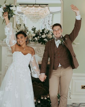 Bride in a floral wedding dress and the groom in a checkered suit in front of faux wedding flower decorations.