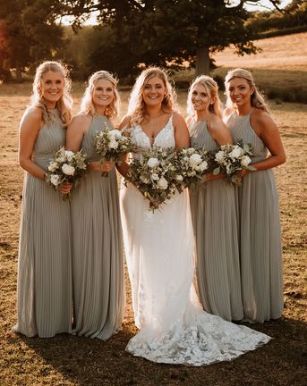 Bridesmaids in sage green pleated bridesmaid dress with the bride for a rustic barn wedding.