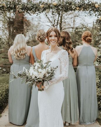 Bride in Maggie Sottero wedding dress holding white wedding flowers with eucalyptus bouquet and bridesmaids in sage green dresses with matching bouquets.