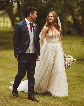 Bride in sparkly Pronovias strapless wedding dress with groom in blue suit and red tie walking together on their wedding day.