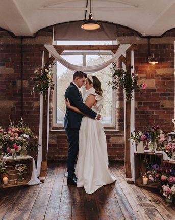 Bowers Mill wedding venue with industrial elements and pretty wildflower decor arranged by the bride herself. Bride wears Jesus Peiro gown and groom wears blue suit.
