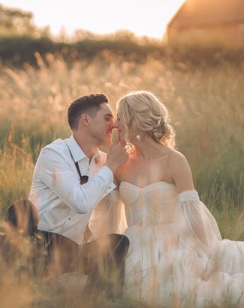 Bride and groom sitting in grass during golden hour at barn wedding