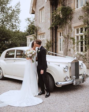 Bride and groom kissing in front of white wedding car at the Casterton Grange Estate venue.