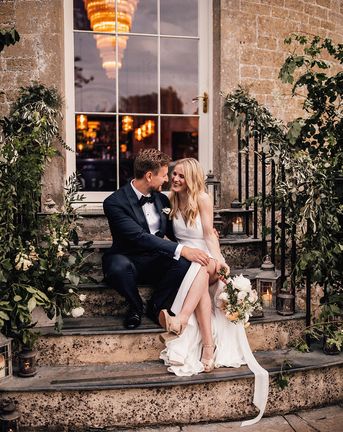 Bride and groom sit smiling on the stairs for their Babington House wedding.