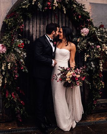 Bride in a beaded sparkle wedding dress with the groom in black tie surrounded by pink flowers.