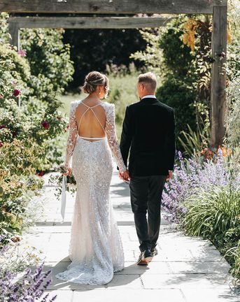Bride in 3D lace wedding dress with an open back walking with the groom in black tie.