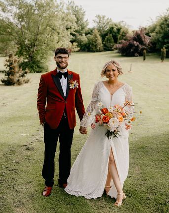 Bride holding an orange and yellow wedding flower bouquet in a boho dress with groom in an orange tux