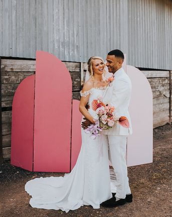 Bride and groom laugh together in front of their DIY pink wedding screen background.