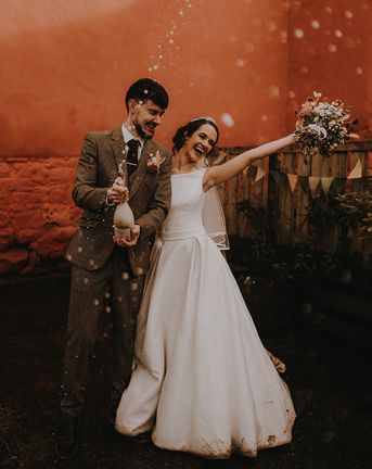 Rustic romance wedding theme for Devon wedding with the bride and groom popping champagne.