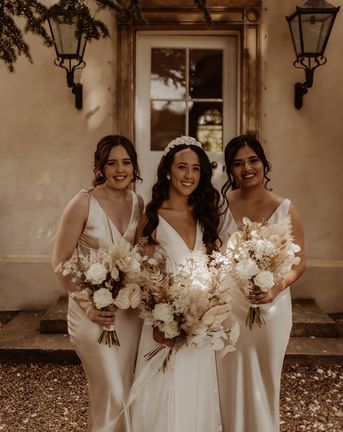 Bride in Alexandra Grecco wedding dress with white flower bridal headband and bridesmaids in champagne gold satin dresses.